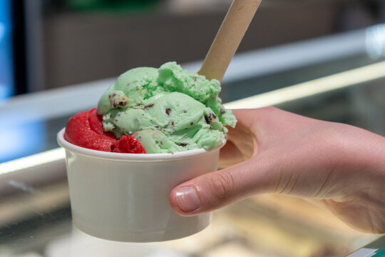 Person holding colorful gelato cup near ice cream display counter