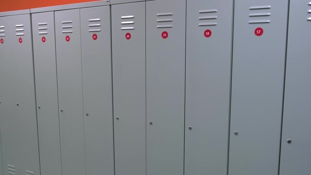 Lockers in in gym fitness locker room or school hallway. Locker row with tiled floor. Gray metal lockers. Hall Interior. No people. Real video. Stainless steel Lockers with number plates for storage.