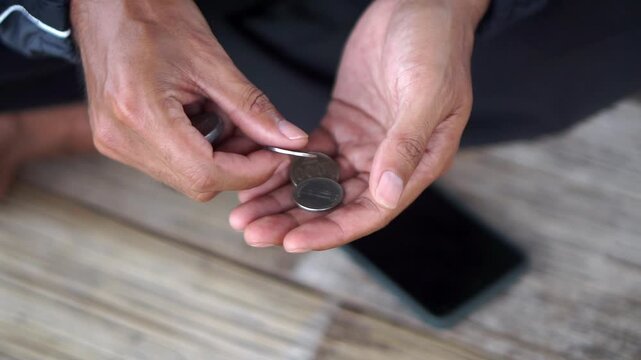 Detailed footage of a man's hands sorting and counting rupiah coins as an illustration of daily finances.