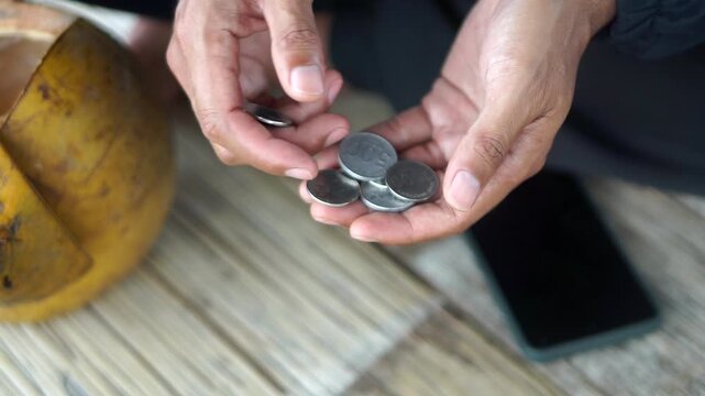 Detailed footage of a man's hands sorting and counting rupiah coins as an illustration of daily finances.