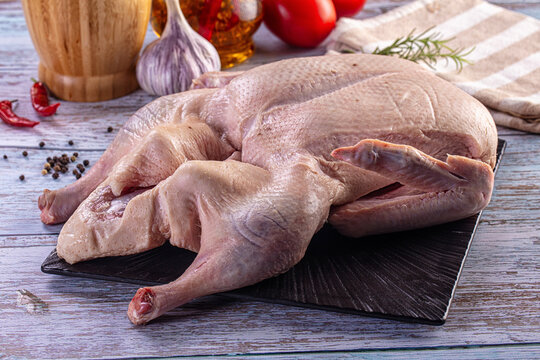 Whole raw duck prepared for roasting with fresh herbs, garlic, and spices on a rustic wooden table