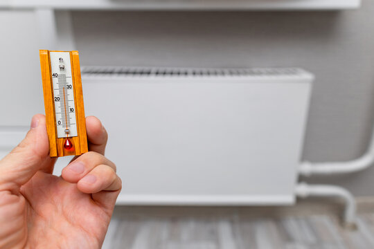 a man's hand holding a room thermometer. measuring room temperature. heat at home. heating season. high air temperature in the room. measuring the air temperature near a heating radiator