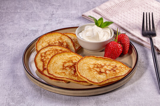 Golden pancakes with fresh strawberries and sour cream on gray background