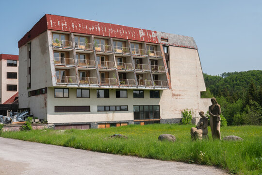 View of the abandoned hotel Junior in Krpacovo with its decaying facade and balconies overlooking a green meadow with stone statues in Dolna Lehota, Banskobystricky kraj, Slovakia.