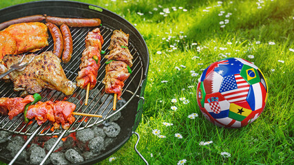  Delicious grilled meat with vegetables sizzling over the coals on barbecue with a soccer covered with multiple national flags symbolizing an international football tournament. © Igor Link
