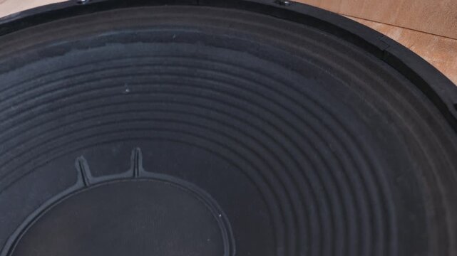 A large black paper audio speaker cone vibrates while playing bass frequencies. The ribbed texture of the subwoofer diffuser is visible in close detail. Sound waves generate pressure.