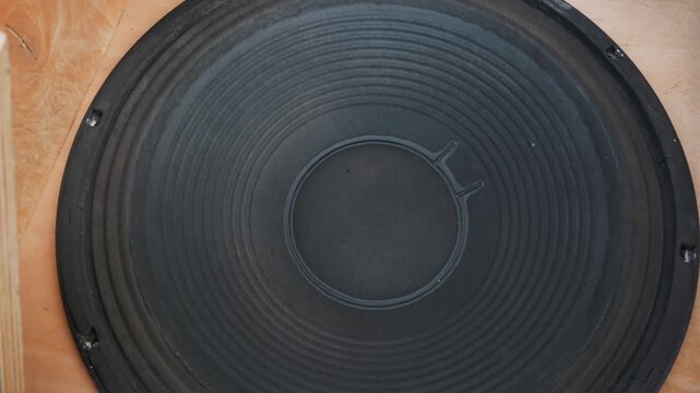 Close up of a large black paper speaker cone vibrating rapidly while playing loud music. Visualizes the concept of intense sound pressure, heavy bass frequencies, and powerful acoustics.