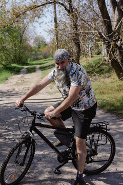 An elderly man rides a bicycle throught the village. Man with a gray beard. Healthy lifestyle.