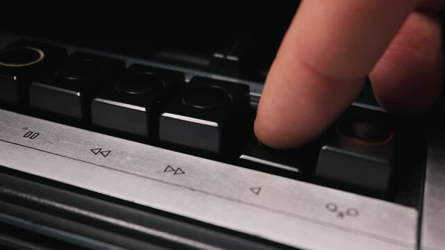 Close up view of a male finger pushing the mechanical play control button on a classic analog vintage audio cassette tape recorder deck. The concept represents retro media technology.