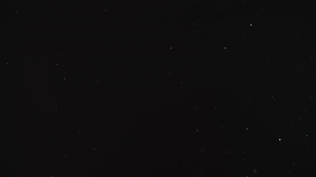 Slow motion real dust particles floating mid air over dark background