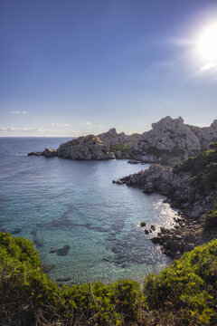 View of the granite rock formations and turquoise sea with Mediterranean scrub under a bright sun Capo Testa, Cala Spinosa, Sardegna, Italy.
