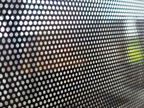 Close macro view of perforated mesh hole dot pattern texture creating an abstract background. Light shines through dark surface evoking calm mysterious feeling with blurred soft depth