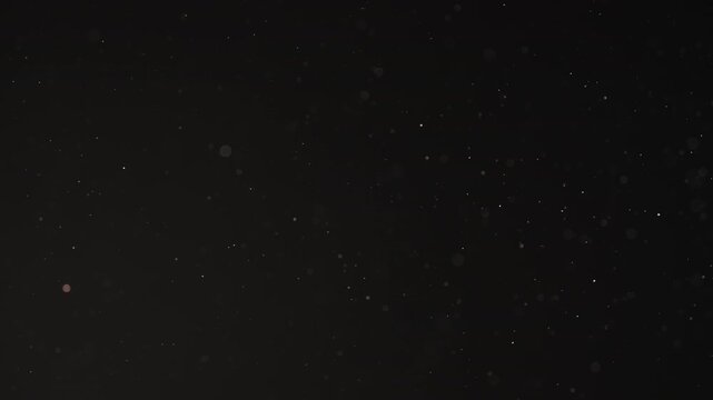 Slow motion real dust particles floating mid air over dark background