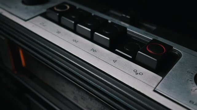 A close-up view of a person finger pressing the record button with a red circle on a vintage stereo. The classic retro audio equipment features metallic details and mechanical push buttons.