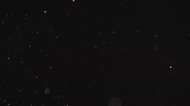 Slow motion real dust particles floating mid air over dark background