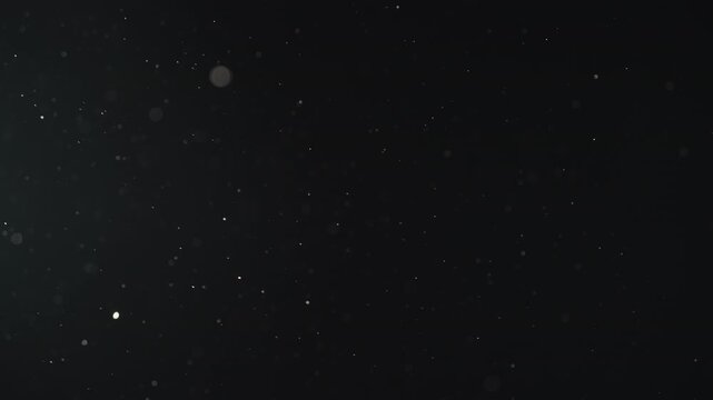 Slow motion real dust particles floating mid air over dark background