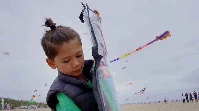 Child preparing and checking a kite before flying it on a beach, focused and engaged in outdoor recreational activity.