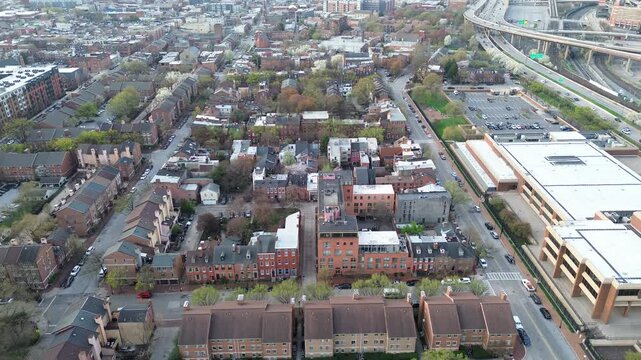 Highway edge housing blocks near MLK Jr Blvd sit beside elevated interchange ramps, large white roof complex. Varied shingles, brick patterns appear under even midday lighting Baltimore, MD