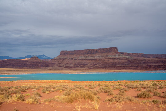 View of bright blue potash evaporation ponds and red rock mesas under a cloudy sky in Moab, Utah, United States.