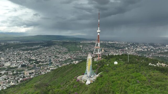 Aerial view of the Funicular Restaurant at Mtatsminda Park during sunset. Dynamic drone shot of a TV tower with Tbilisi city in the background.