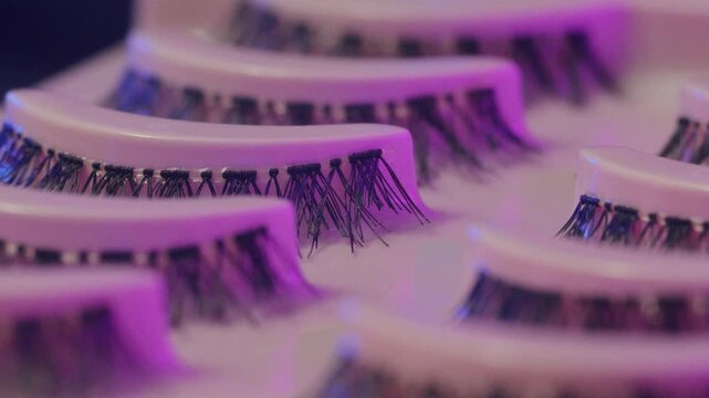 Synthetic false lashes illuminated by vibrant neon lighting. Modern studio setup highlights delicate fibers and glossy packaging in glamorous beauty retail scene
