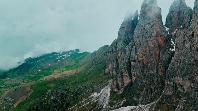 Aerial view of rugged Seceda rock formations with steep cliffs and alpine slopes. Dramatic Dolomites terrain with clouds