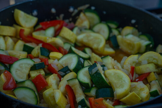 View of fresh sliced zucchini, yellow squash, red bell peppers, and chopped onions sauteing in a pan in Moab, Utah, United States.