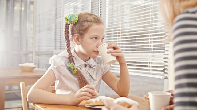 Girl with pigtails eats cakes with her mum in the cafe