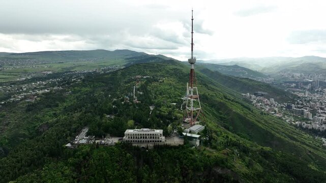 Aerial view of the Funicular Restaurant at Mtatsminda Park during sunset. Dynamic drone shot of a TV tower with Tbilisi city in the background.
