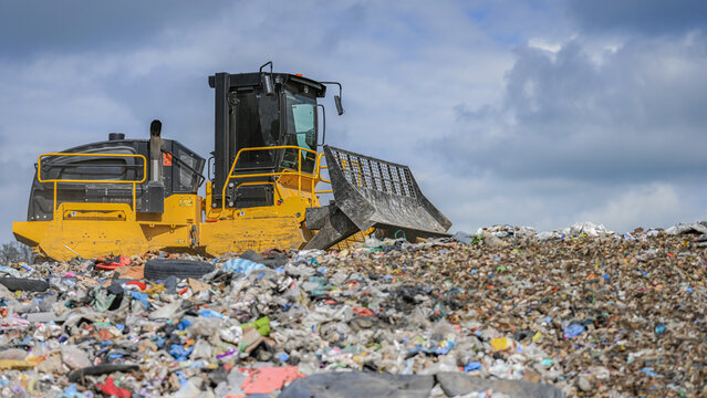 Heavy industrial machinery working at a large landfill site.  A view on a landfill compactor compacting and managing piles of waste.