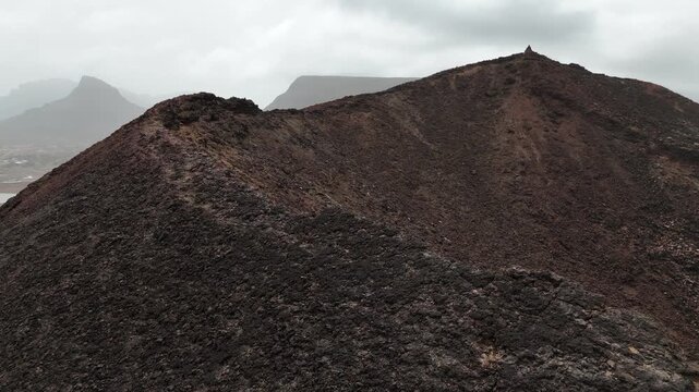 Close-up aerial view of the dark, scoriaceous rim of a volcanic crater near Calhau Village, Sao Vicente. A moody drone shot of the rugged volcanic ridges and desolate peaks of Cabo Verde