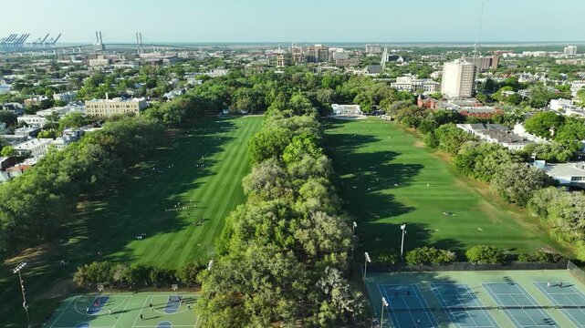 Cinematic bird's-eye shot of Forsyth Park in the heart of Savannah, featuring the iconic bandshell, sprawling open fields, and visitors relaxing under the southern sun.