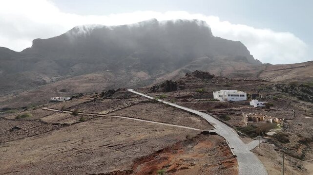 Aerial drone view of a winding asphalt road crossing the misty volcanic slopes of Monte Verde, Sao Vicente. Low clouds cover the highest peaks of the Cabo Verde islands during a gray day