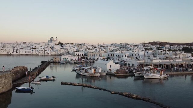 Drone shot of old port of Naousa, cycladic whitewashed houses, bustling Venetian harbour at sunset, Paros, Aegean sea