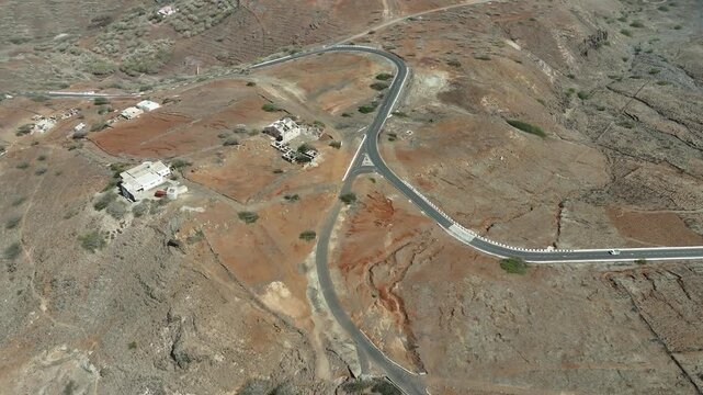 High-angle drone perspective of a solitary asphalt road curving through the barren, reddish-brown slopes of Monte Verde. A stark look at the remote volcanic infrastructure in Sao Vicente