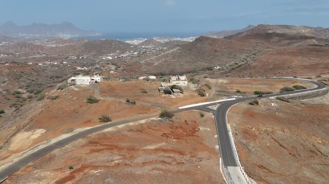 Drone view of small white buildings and a winding road situated on the high volcanic plateaus of Monte Verde. A glimpse into the isolated mountain life and rural outposts of Cabo Verde