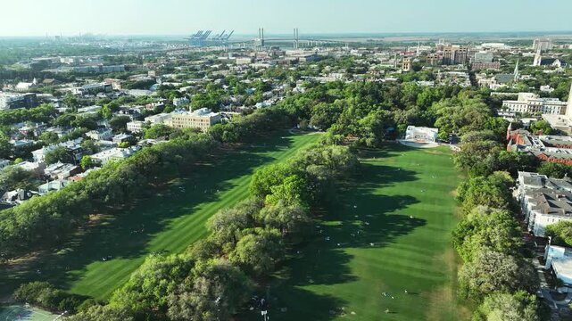 High-altitude aerial of Forsyth Park in Savannah, Georgia, with picnickers spread across the lawn, the historic stage, and centuries-old live oaks framing the scene.