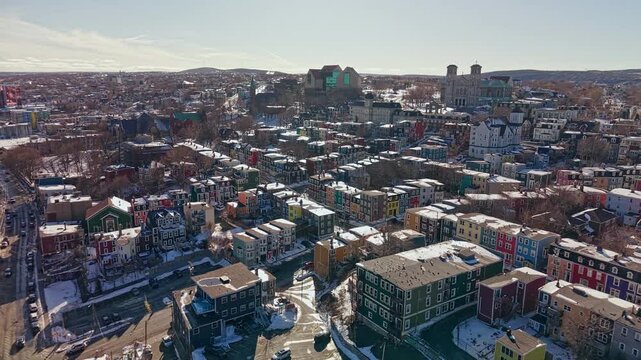 Aerial drone view of colorful jellybean row houses in St Johns Newfoundland during winter with snow covered rooftops and churches in background
