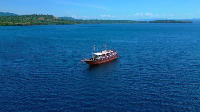 Traditional phinisi boat on open water with a person jumping off the bow into the sea. Lovely aerial view fly push forward panorama drone