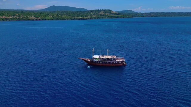 Traditional phinisi boat on open water with a person jumping off the bow into the sea. Best aerial view fly push forward panorama drone