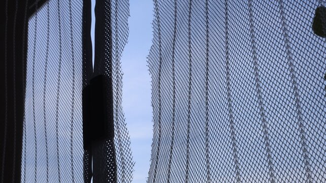 A tear in a fly screen, close-up of a torn mosquito net against a clear sky