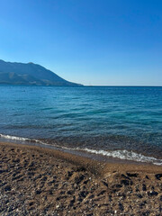 Fototapeta premium Pebbly shoreline meeting calm sea with distant mountain view