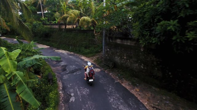 Aerial view of a couple riding a scooter on a bumpy asphalt road through a tropical jungle