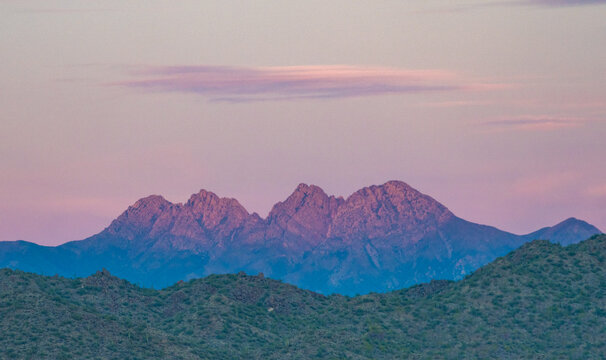 View of Four Peaks mountain range with jagged summits under a soft pink and purple sunset sky with desert hills in the foreground Arizona, United States.