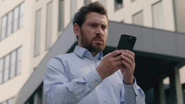 Mad unhappy European middle aged businessman using smartphone in city angry male employer annoyed frustrated by bad signal spam message irritated mature business man outdoor work mobile phone daylight