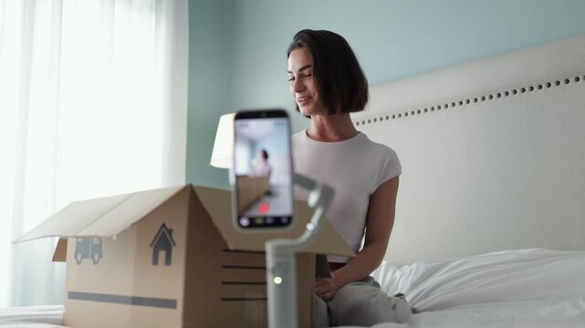 Woman recording product reveal from cardboard package using smartphone camera. Concept online retail and social media trends.
