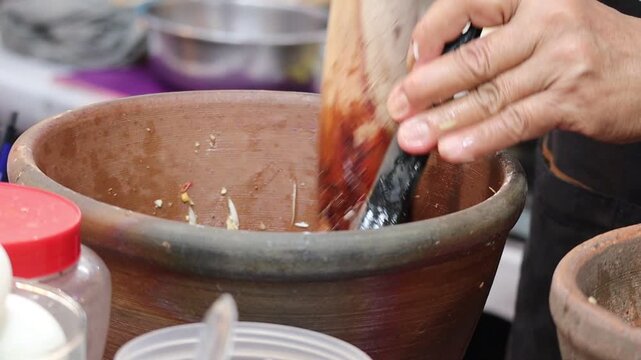 Close-up of a person using a traditional wooden pestle and clay mortar to prepare Thai papaya salad (Som Tum).