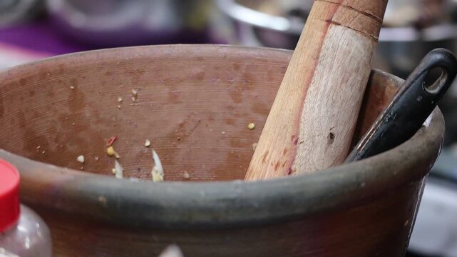 Close-up of a person using a ladle and traditional wooden pestle in a clay mortar to mix ingredients for Thai papaya salad (Som Tum).