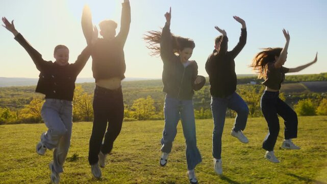 Group of five happy friends running and jumping on a hill toward camera