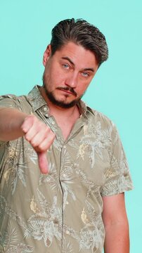 Man first shows thumbs up then quickly switches to thumbs down, expressing disagreement and confusion. Young adult guy demonstrates emotional change of opinion with mixed reaction on blue background